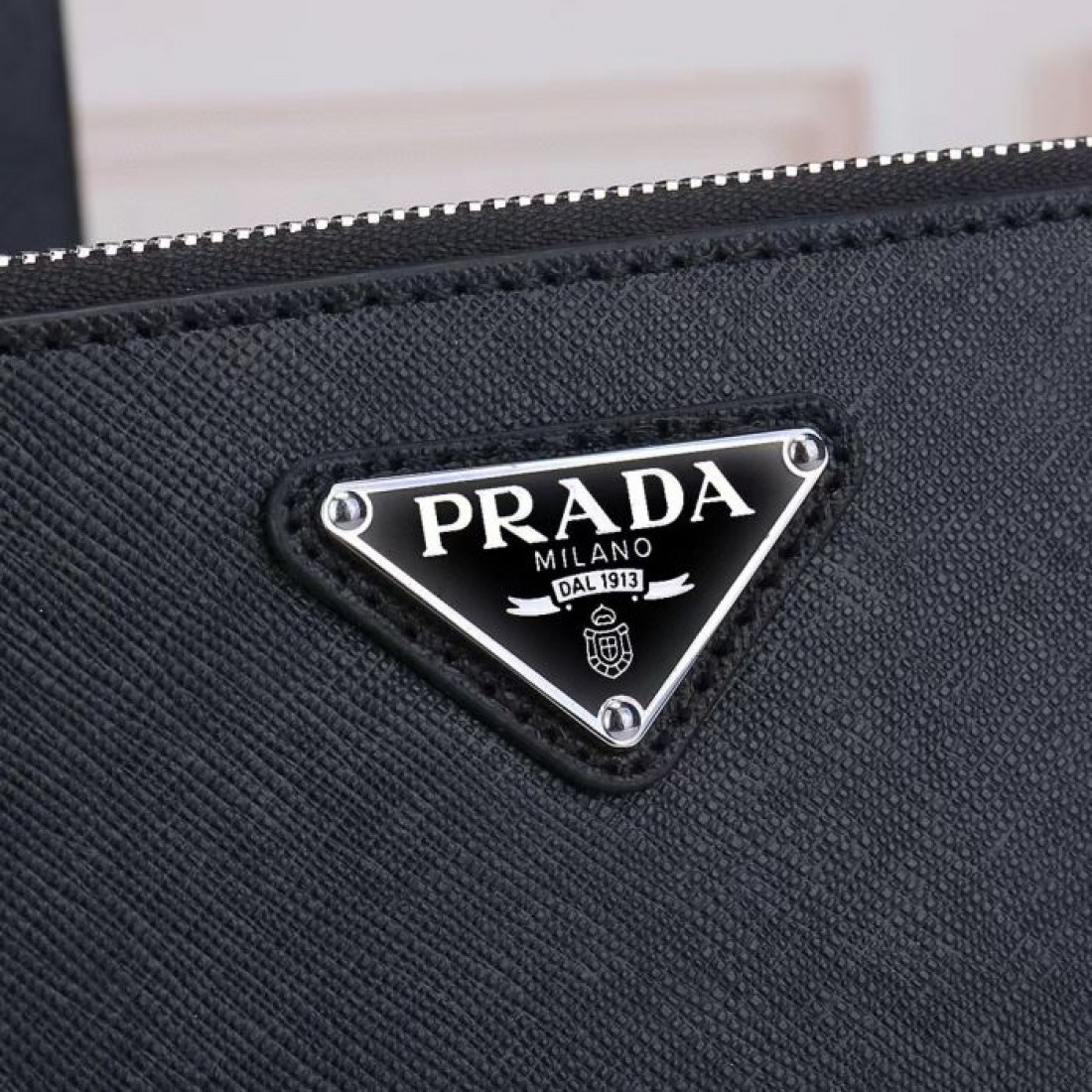 シンプルながら存在感のある黒のPRADAプラダコピークラッチバッグラウンドファスナーと控えめなロゴが際立つ都会的なメンズカジュアル小物